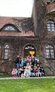Grupa 20 dzieci w wieku przedszkolnym wraz z 2 paniami pozuje do zdjęcia na schodach zamku w Gutowie.