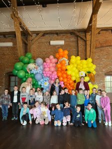 Grupa 20 dzieci w wieku przedszkolnym pozuje do zdjęcia na tle ścianki z balonów i dmuchanych zajączków na zamku w Gutowie. Na zdjęciu znajdują się również 3 panie nauczycielki grupy.