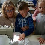 Dwójka dzieci przy maszynie do szyci obserwuje jak nauczycielka szyje materiał