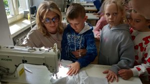 Dwójka dzieci przy maszynie do szyci obserwuje jak nauczycielka szyje materiał