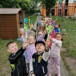 Grupa dzieci unosi w ręce otrzymane bańki mydlane stojąc na przedszkolnym placu zabaw