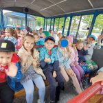 Grupa dzieci siedzi w kolejce turystycznej czekając na wyjazd.