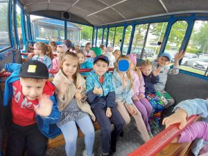 Grupa dzieci siedzi w kolejce turystycznej czekając na wyjazd.