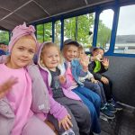 Trzy dziewczynki i dwóch chłopców siedzi w kolejce turystycznej, machają.