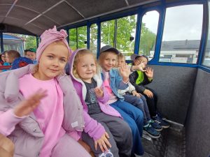 Trzy dziewczynki i dwóch chłopców siedzi w kolejce turystycznej, machają.