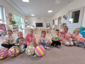 Pięć dziewczynek i dwóch chłopców siedzi na dywanie trzymając prezenty.