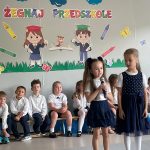 Dwie dziewczynki stoją i recytują wiersz, reszta dzieci siedzi w tyle na lawkach