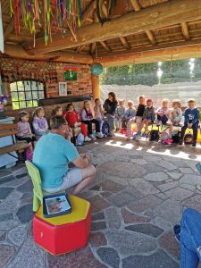 Dzieci siedzą w półkolu na ławkach w altanie i słuchają Pana opowiadającego o zwierzętach