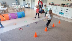Dzieci przechodzą przez slalom sportowy ustawiony w sali.
