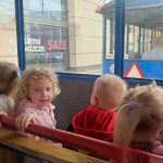 Dzieci siedzą na drewnianych ławkach wagonu kolejki i patrzą przez okna na ulice miasta.