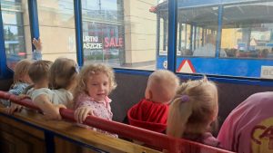 Dzieci siedzą na drewnianych ławkach wagonu kolejki i patrzą przez okna na ulice miasta.