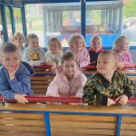 Dzieci klęczą na drewnianych ławkach w środku wagonu kolejki.