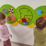 Chłopiec i dziewczynka kręcą rączkami kolorowe kółka zawieszone na ścianie.