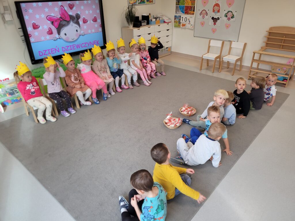 Dziewczynki siedzą na krzesłach ustawionych w rzędzie, a chłopcy naprzeciw nich.