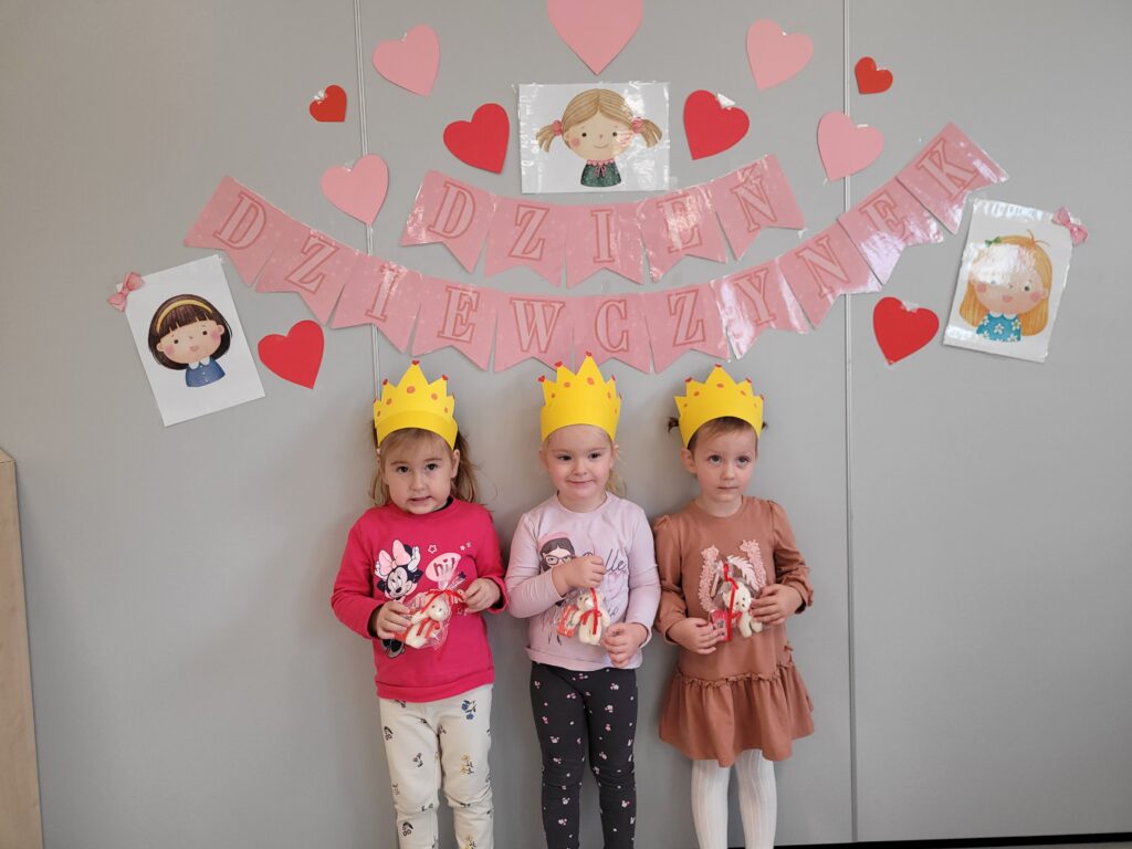 Trzy dziewczynki stoją na tle dekoracji z okazji Dnia Dziewczynki