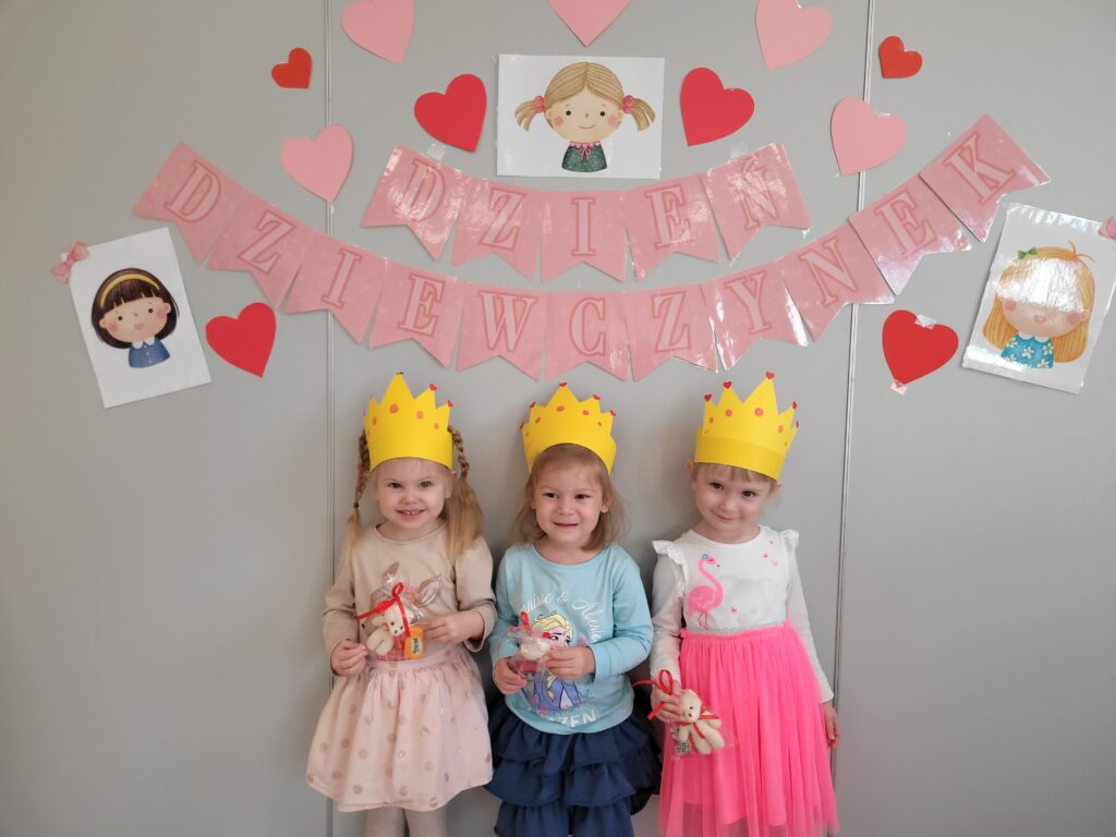 Trzy dziewczynki stoją na tle dekoracji z okazji Dnia Dziewczynki