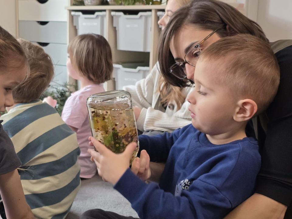 DZIECKO TRZYMA W RĘCE SENSORYCZNY SŁOIK Z DRZEWEM W ŚRODKU