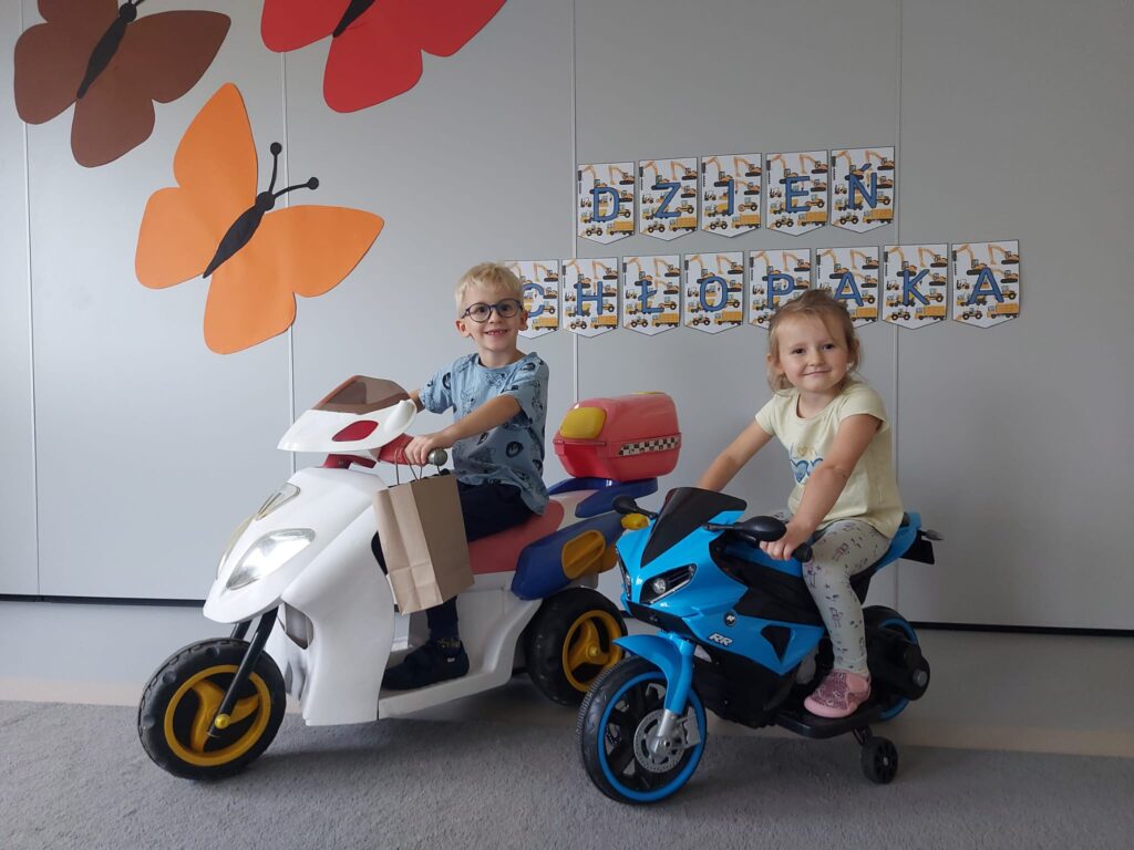 chłopiec siedzi na białym motorze a dziewczynka na niebieskim motorze, które stoją na dywanie