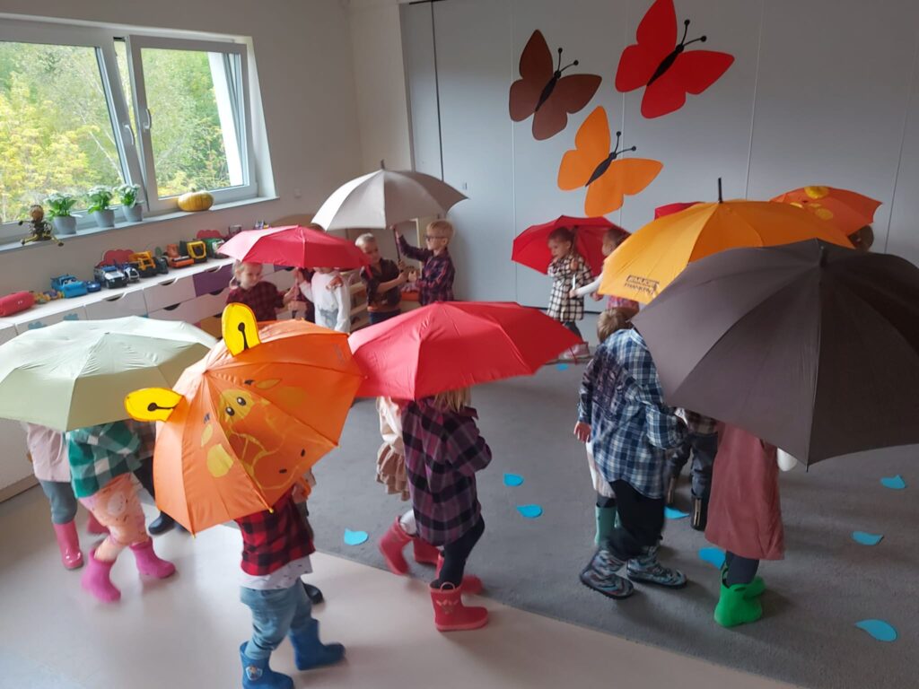 dzieci chodzą w kaloszach po dywanie pod parasolami 