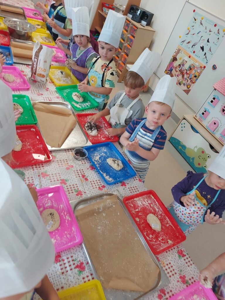 dzieci w strojach kucharzy ugniatają ciasto na chleb, na stoliku są produkty potrzebne do pieczenia chleba