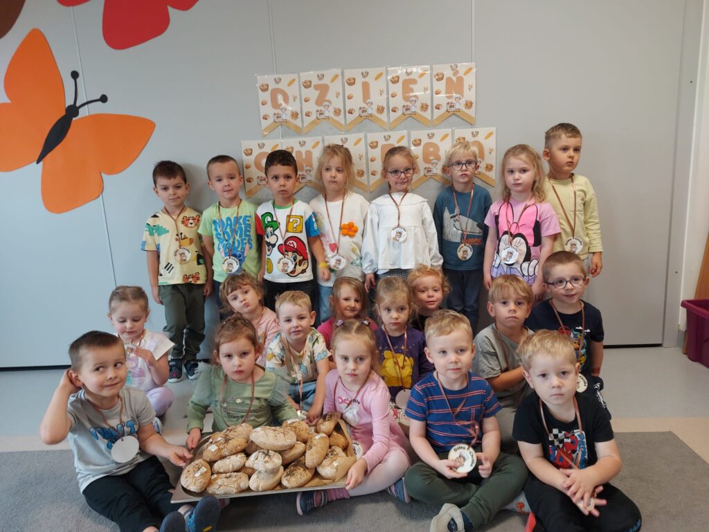 grupa dzieci siedzą na dywanie dzieci trzymają na tacy swoje chlebki