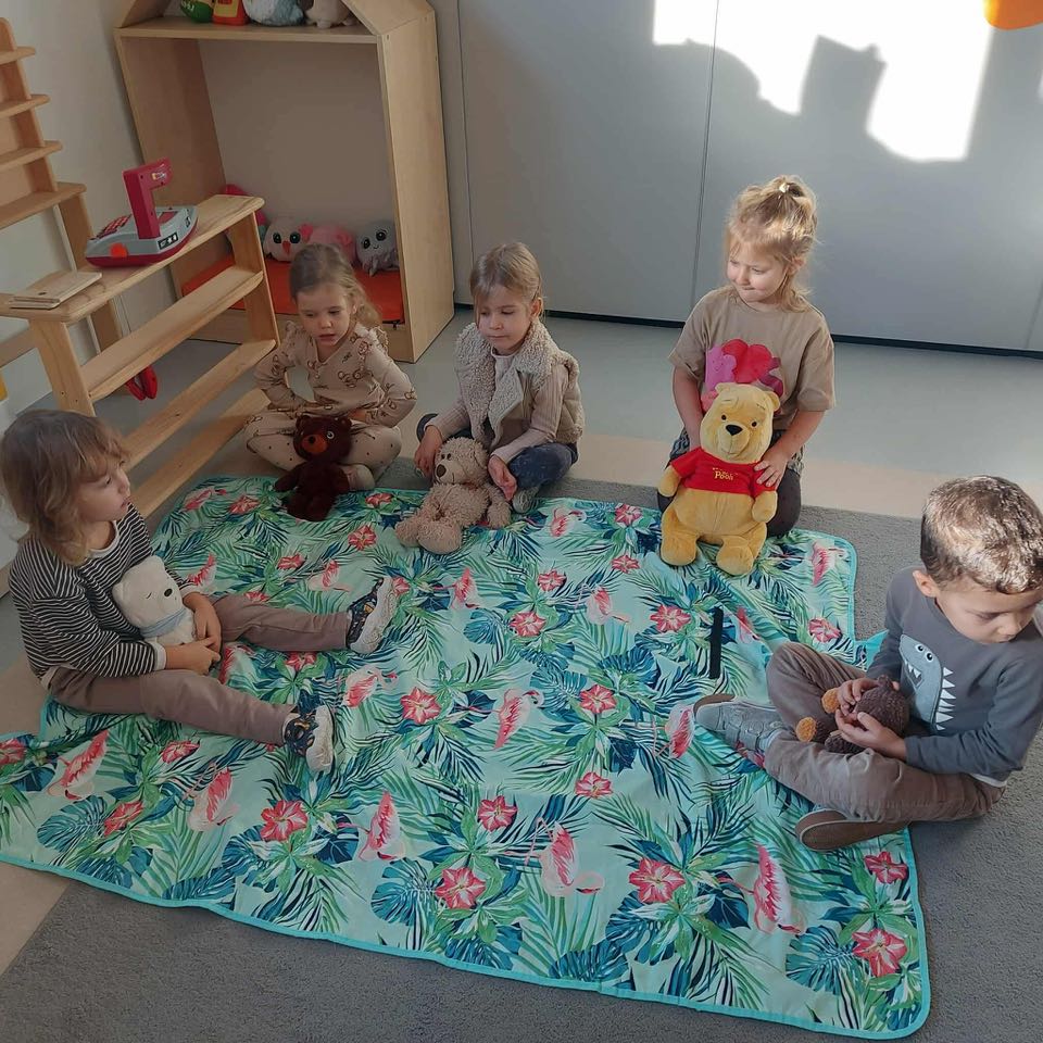 dzieci siedzą na kocu ze swoimi misiami na pikniku