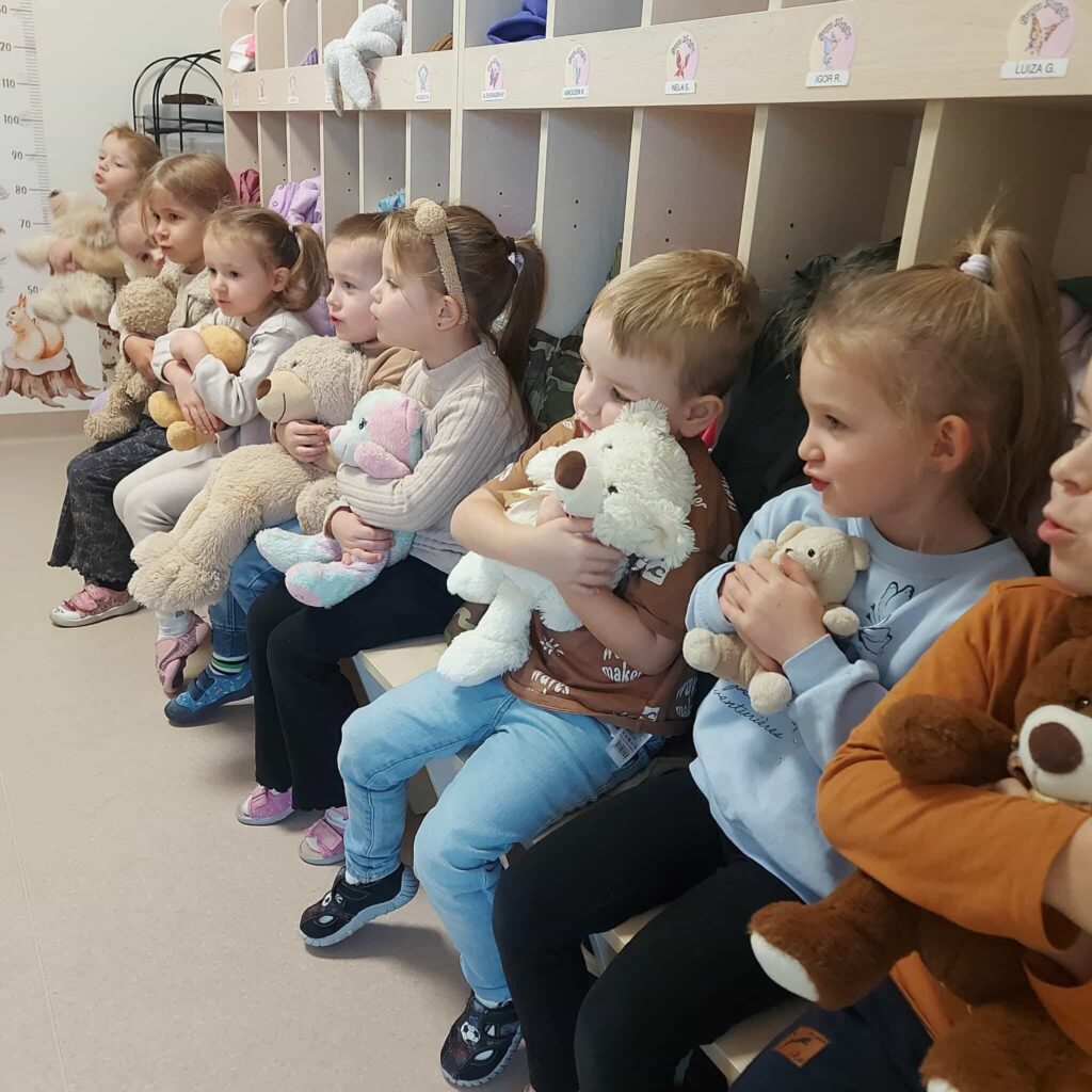 dzieci siedzą na ławeczce i przytulają swoje misie 