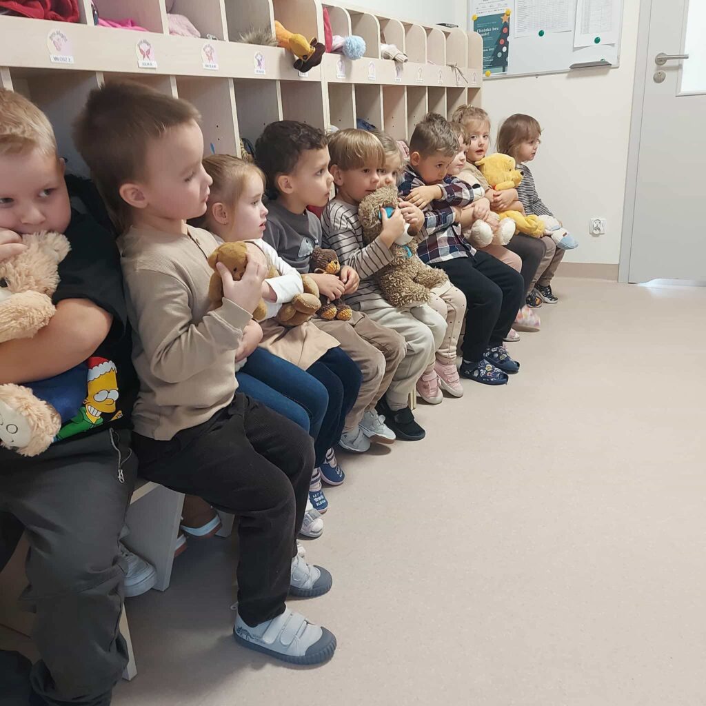 dzieci siedzą na ławeczce i przytulają swoje misie 