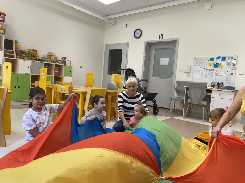 Dzieci siedzą na dywanie w rękach trzymają kolorową chustę animacyjną