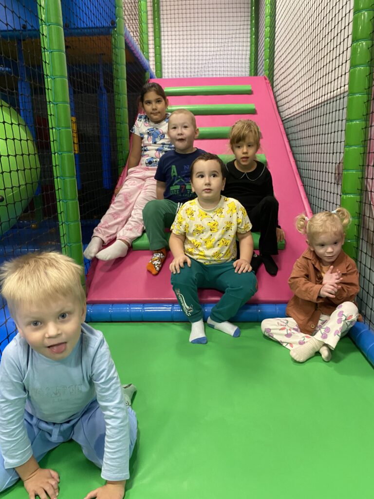 3 chłopców i 3 dziewczynki siedzą na materacu w sali zabaw.