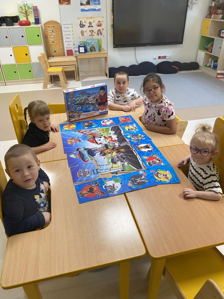 Dzieci przy stoliku układają puzzle.