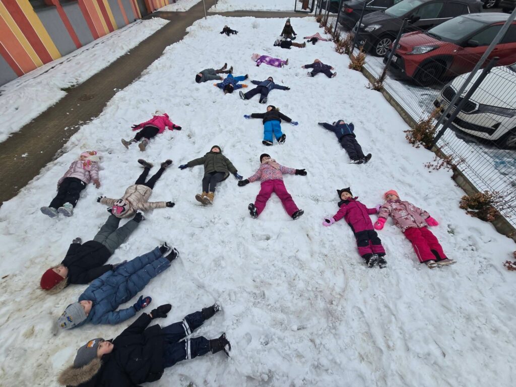 Duża grupa dzieci leży na plecach na białym śniegu.