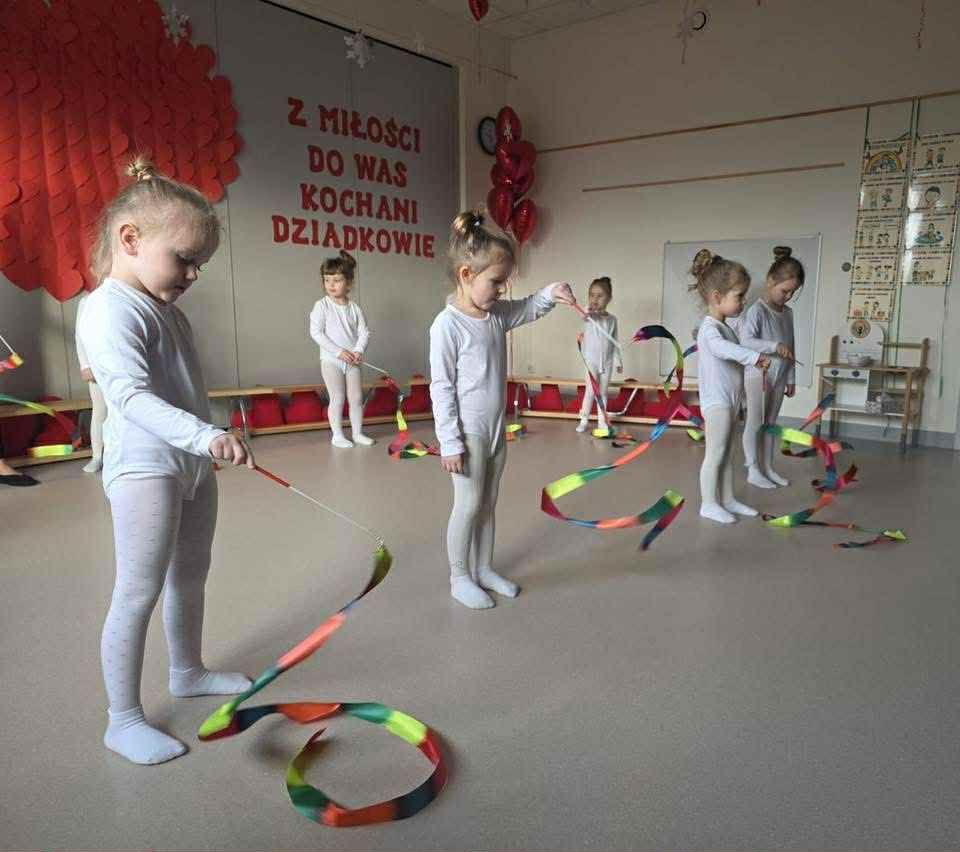 dziewczynki ubrane na biało tańczą z kolorowymi szarfami