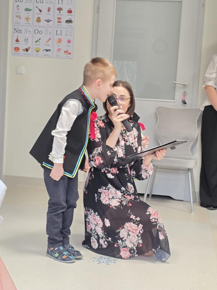 Chłopiec stoi obok nauczyciela recytując wierszyk dla Babci i Dziedka.