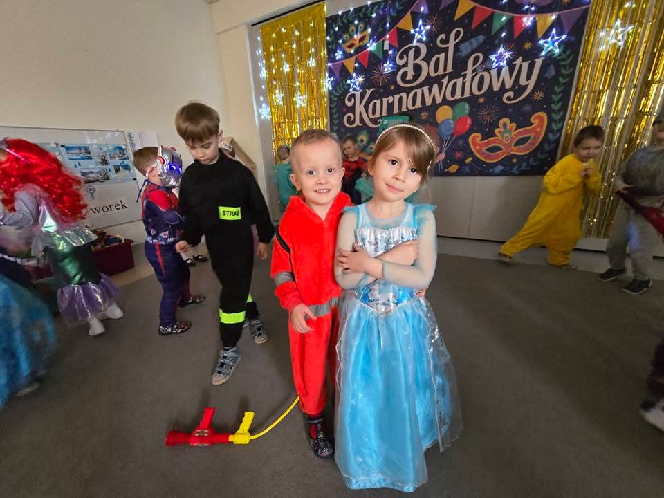 Dwoje dzieci przebranych w stroje karnawałowe tańczy i pozuje do zdjęć w trakcie balu karnawałowego.