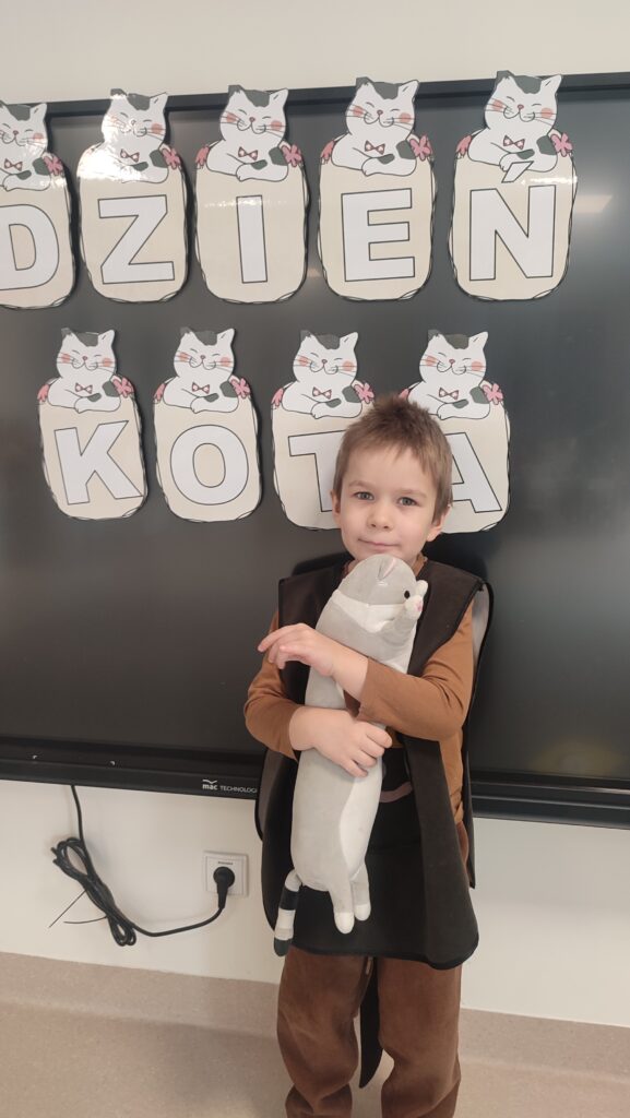 Chłopiec przebrany w strój kota w rękach trzyma maskotkę kota, do której się przytula.