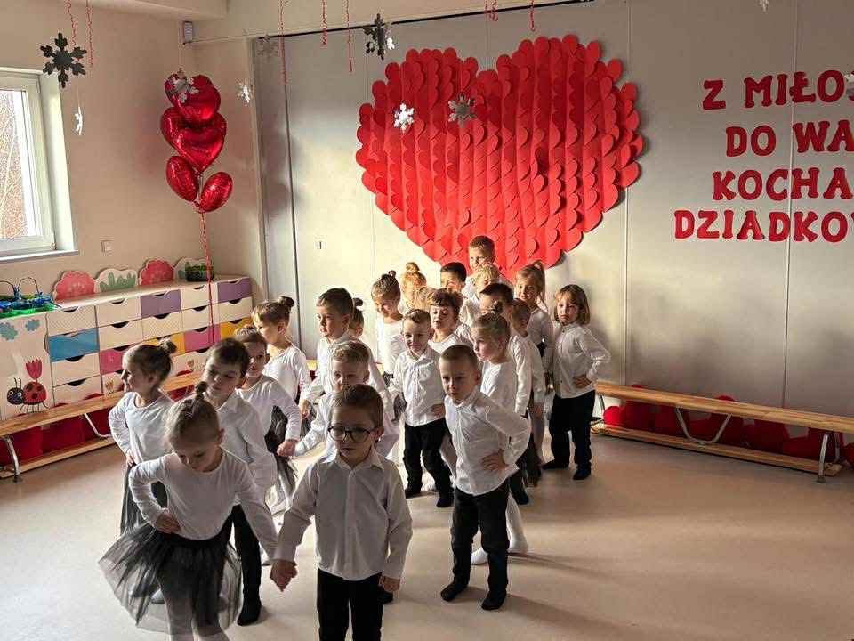 dzieci ubrane w biało-czarne stroje są ustawione parami na środku sceny