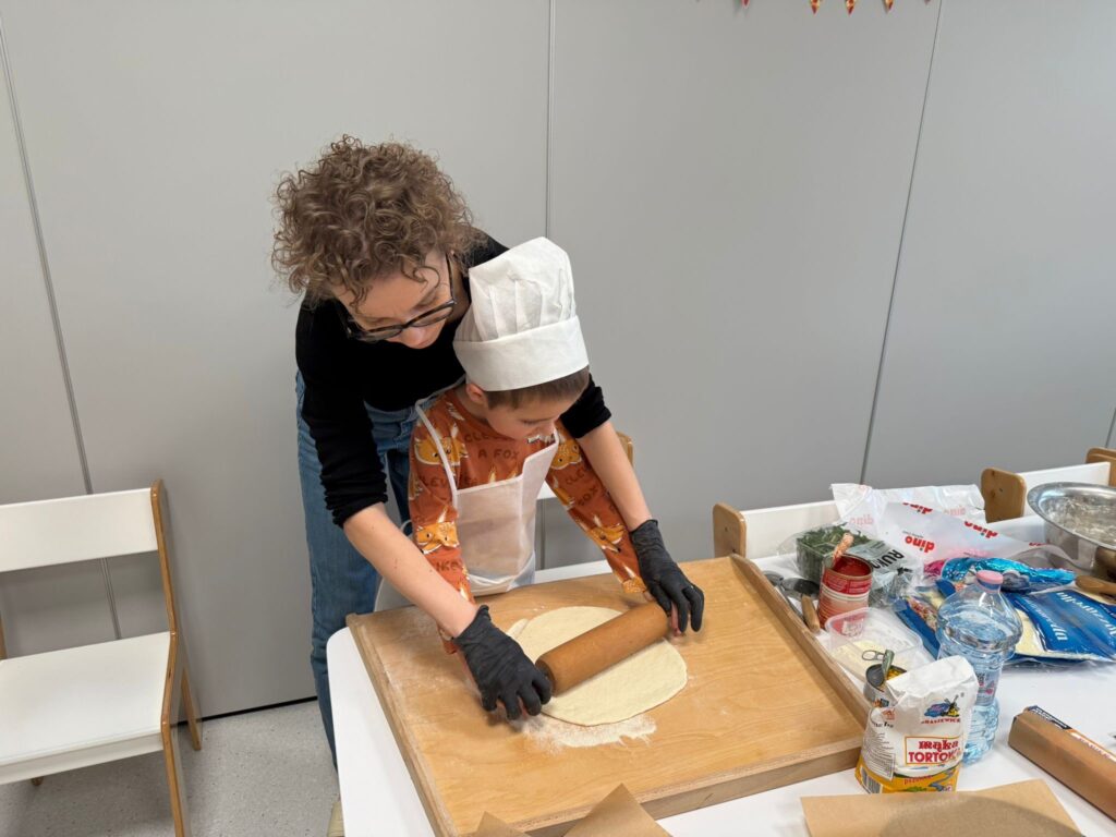 Chłopiec z pomocą nauczyciela rozwałkowuje ciasto na pizzę.