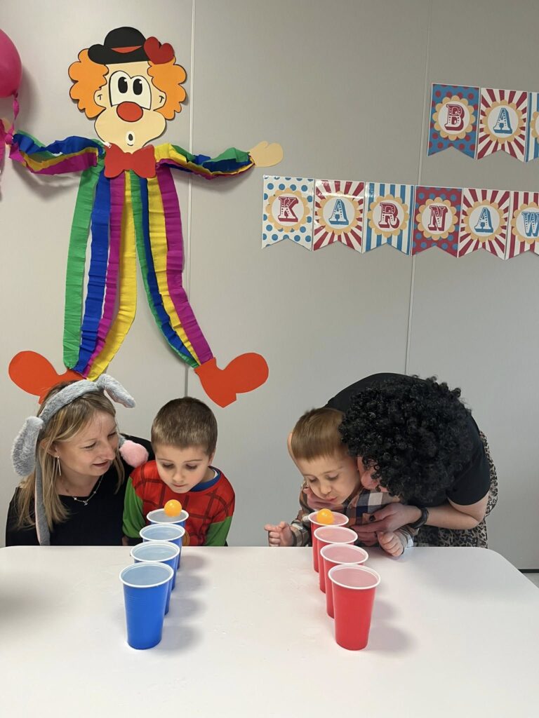 Dzieci biorą udział w konkurencji, której zadaniem jest przesunięcie piłeczki dmujachąc w nią po powierzchni wody z jednego kubeczka do drugiego.