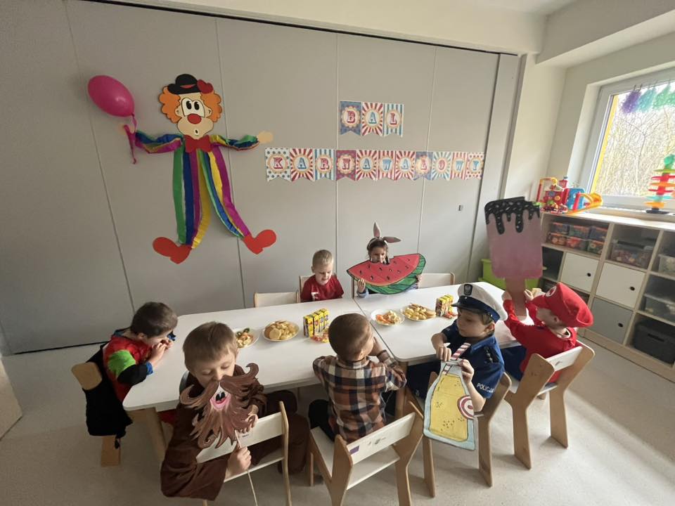 Dzieci siedzą przy stolikach i zjadają słodki poczęstunek.