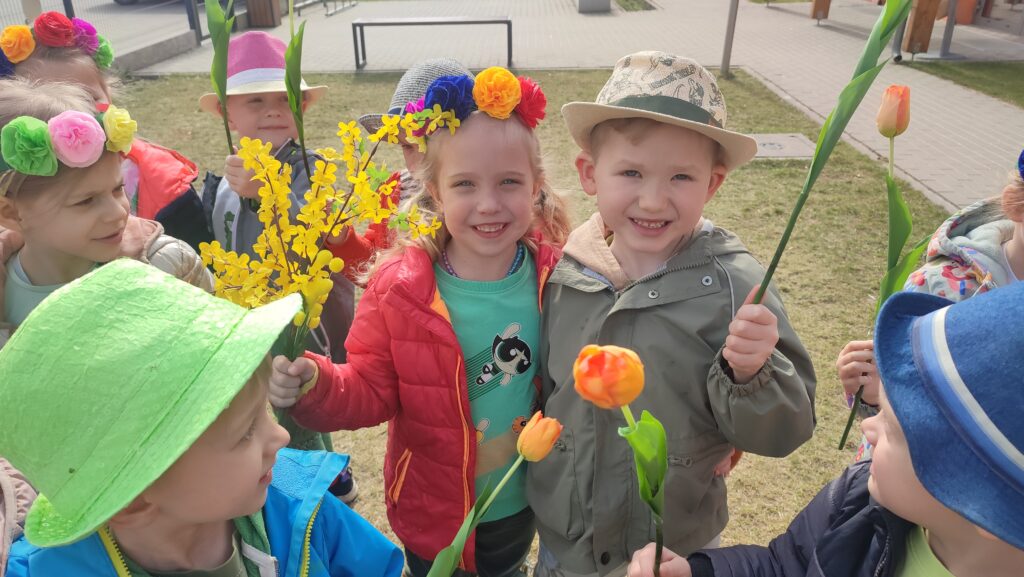 Dziewczynka i chłopiec trzymają w ręce tulipany, forsycje, kwiatki. Pozują do zdjęcia.