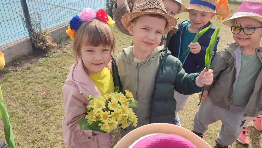 Dziewczynka i chłopiec trzymają w ręce tulipany, forsycje, kwiatki. Pozują do zdjęcia.