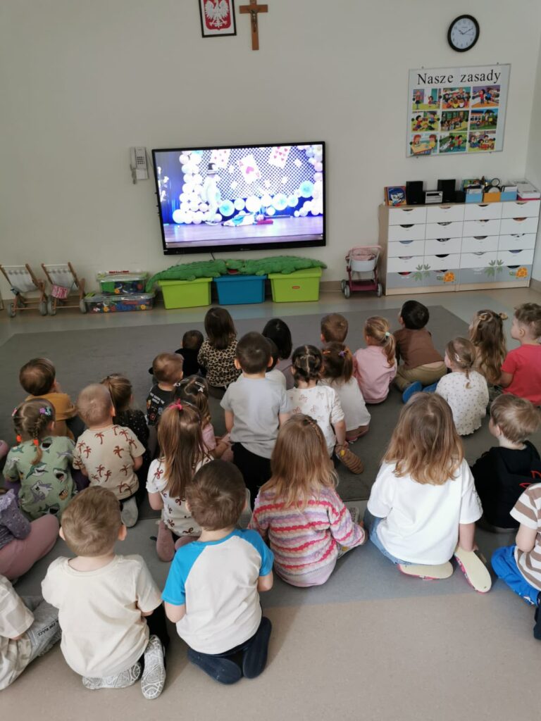 Dzieci siedzą na dywanie i oglądają spektakl