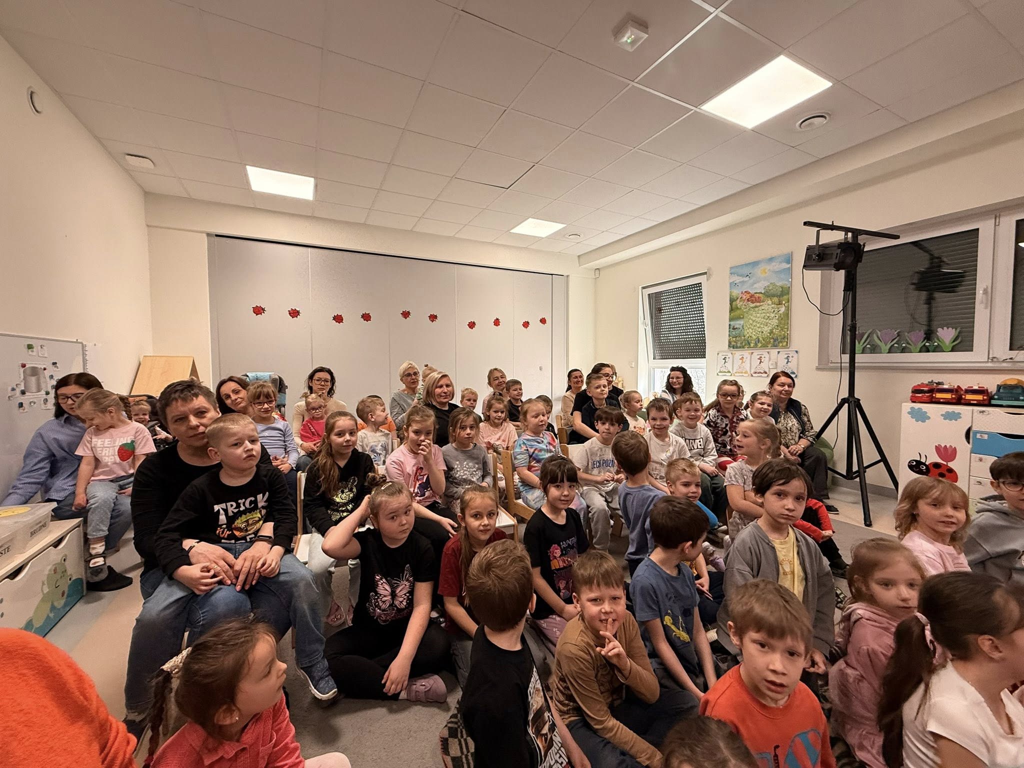 Dzieci siedzą na dywanie i oglądają występ iluzjonisty.