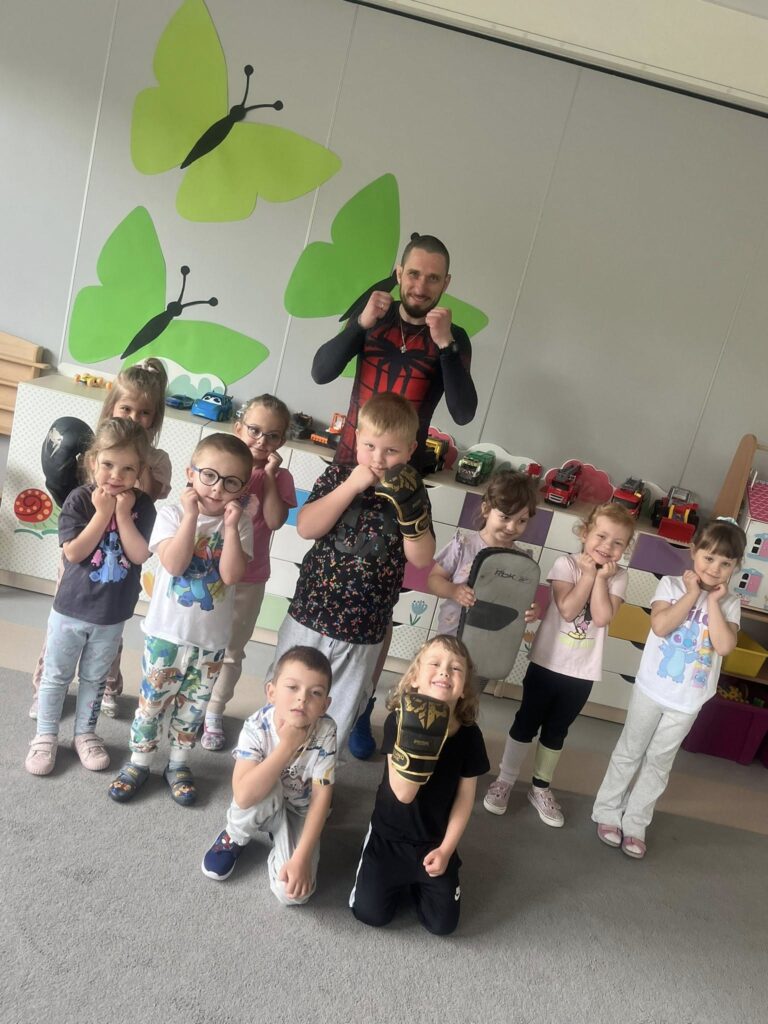 Dzieci w rękawicach pokazują gardę, obok stoi trener