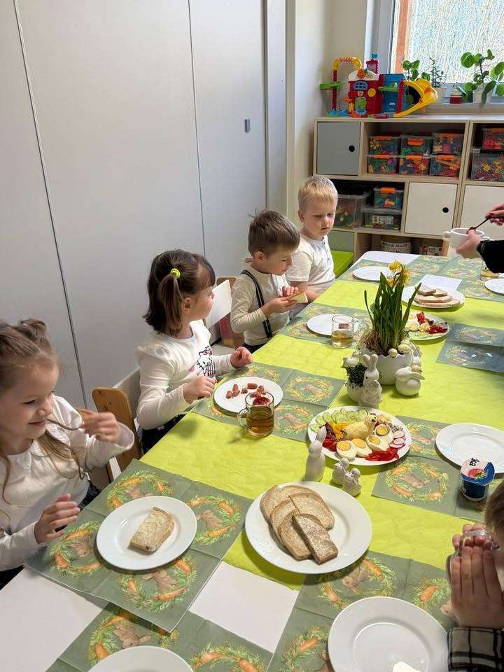 DZIECI SIEDZĄ PRZY STOLE I JEDZĄ WIELKANOCNE ŚNIADANIE