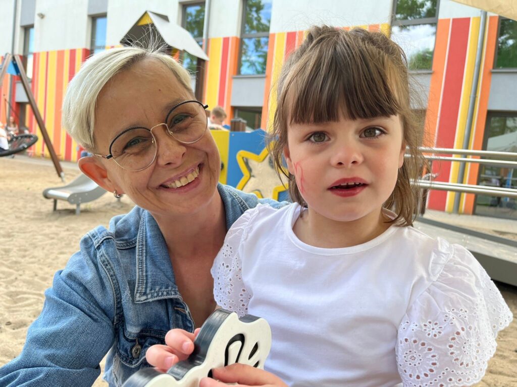 Uśmiechnięta dziewczynka ubrana w białą bluzeczkęsiedzi na huśtawce.