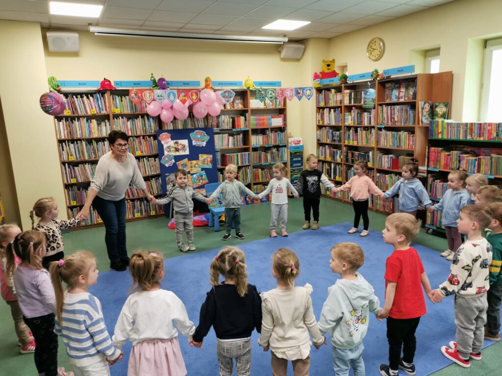 Dzieci tańczą w kole z Panią bibliotekarką
