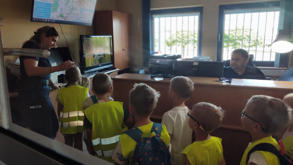 Grupka dzieci stoi w pomieszczeniu, w którym znajdują się monitory i kamery.
