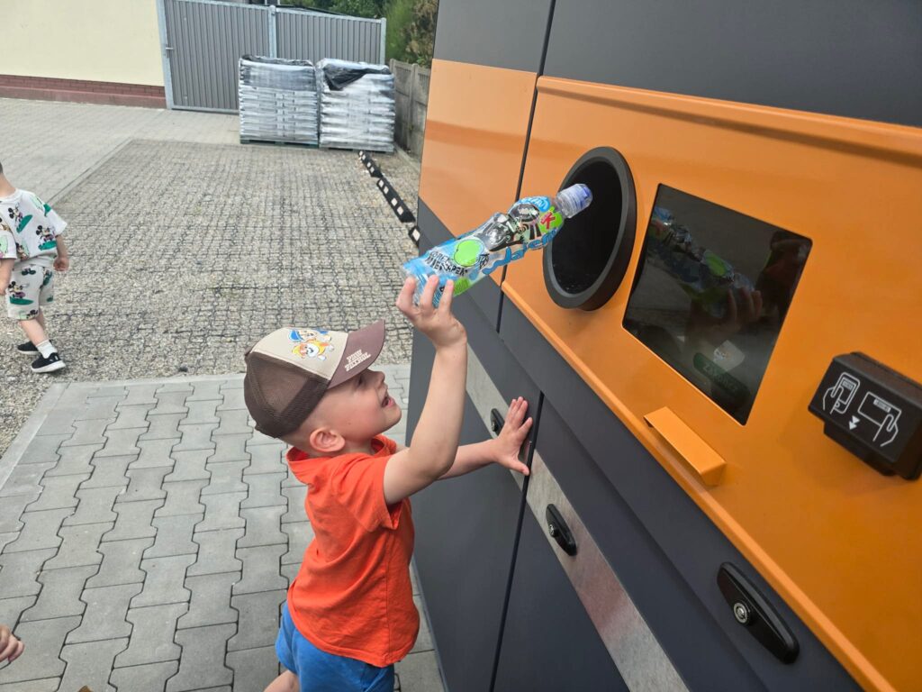 Dziecko stoi przed butelkomatem i wrzuca butelkę do otworu.